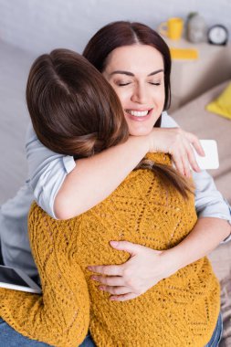 Dijital tablet tutan ve mutlu annesiyle kucaklaşan genç bir kız.