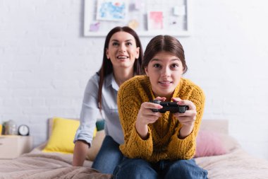 KYIV, UKRAINE - 20 Kasım 2020: Arkaplanda heyecanlı bir annenin yanında joystick tutan genç bir kız