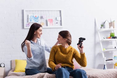 KYIV, UKRAINE - 20 Kasım 2020: mutlu genç kız yatak odasında heyecanlı annesinin yanında joystick tutuyor.