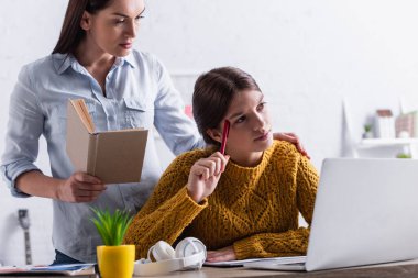 Genç kız ev ödevlerini yaparken kitap ve dizüstü bilgisayarla düşünüyor.