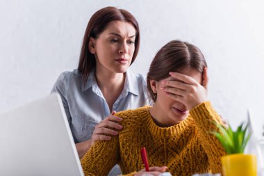 Endişeli bir anne evde internetten okurken kızına sarılıp ağlıyor.