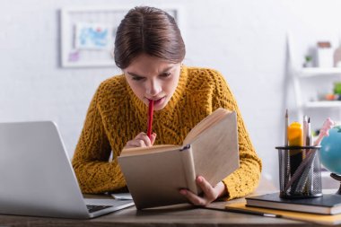 Düşünceli genç kız kitap okuyor ve internetten okurken elinde kalem tutuyor.