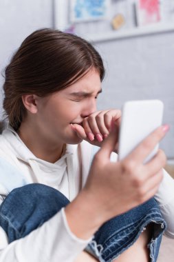 Ağlarken ve elinde akıllı telefon tutarken ağzını kapatan üzgün genç kız. 
