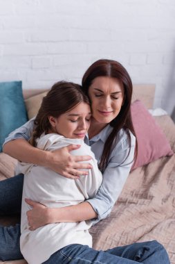 Şefkatli anne, genç kızı yatak odasında kucaklıyor. 