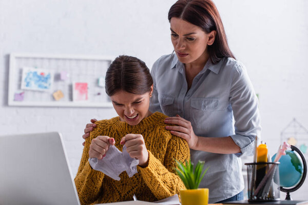 angry teenage girl tearing paper near worried mother
