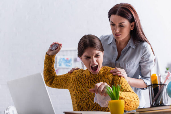 angry teenage girl tearing paper and screaming near worried mother while doing homework 