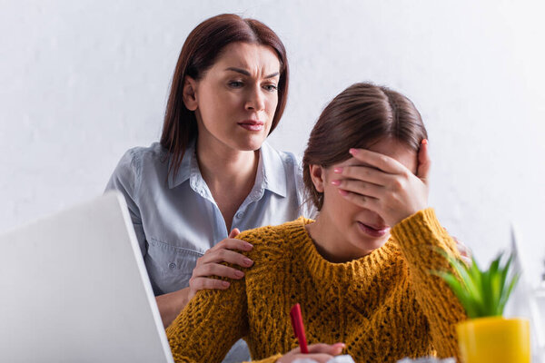 worried mother hugging upset teenage daughter crying while studying online at home