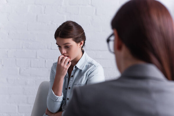 worried teenage girl thinking near psychologist on blurred foreground 