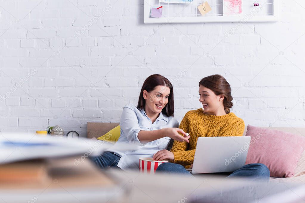 cheerful teenage girl and mother watching comedy movie on laptop in bedroom