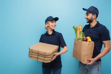 Kese kağıdında yemeği olan mutlu ırklar arası kuryeler ve mavilikte birbirlerine gülümseyen pizza kutuları.