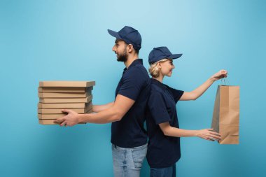 Arap kurye, meslektaşı ile sırt sırta verip mavi üzerine kağıt yapıştırıyor.