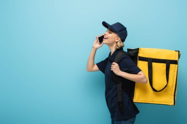 Termo sırt çantalı mutlu kuryenin yan görüntüsü. Akıllı telefondan sırayı kabul ediyor.