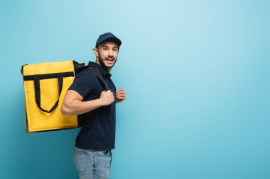 Termal çantalı genç Arap kurye mavi kameraya gülüyor