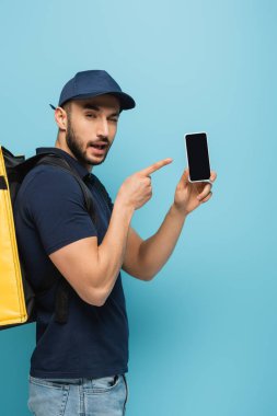 Sırt çantalı sinsi Arap kurye mavi ışıkta cep telefonunu işaret ediyor.