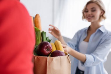 Kuryenin yanında taze yemek ve mutlu bir kadın olan kağıt torbanın seçici odağı. 