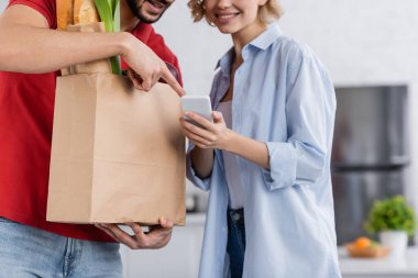 Müşterinin elindeki akıllı telefonu gösteren dağıtım elemanının kırpılmış görüntüsü