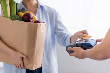 Ödeme terminalini elinde tutan teslimatçının kredi kartı geçmişi bulanık bir kadının yanında görüntüsü.