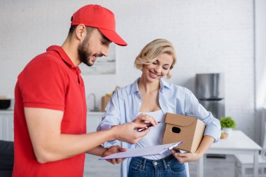 Müslüman kurye, elinde paket olan gülümseyen kadına kalem ve dosya veriyor.