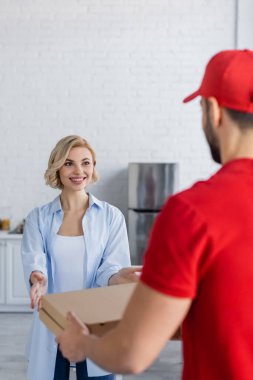 Neşeli, sarışın kadın bulanık önplanda Arap kuryesinden pizza kutuları alıyor.