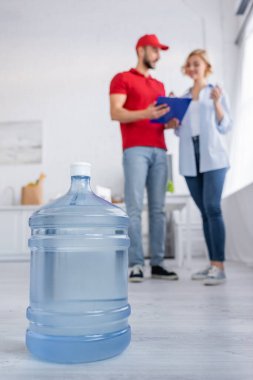 selective focus of big bottle of pure water near arabian courier and woman on blurred background clipart