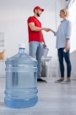 Müslüman kurye ve bulanık arka planda el sıkışan kadının yanında içilebilir büyük bir şişe suyun seçici odağı.