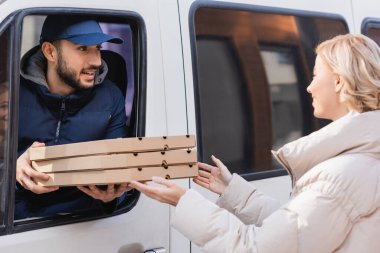 arabian delivery man in truck giving pizza boxes to blonde woman clipart