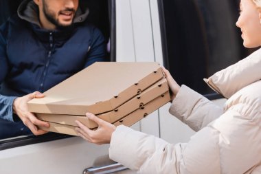 partial view of courier in car giving pizza boxes to woman on blurred background clipart
