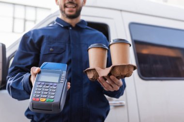 Kahveli teslimatçı görüşü ve bulanık arka planda kredi kartı okuyucusu.