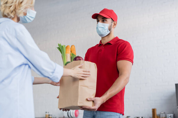 muslim delivery man in medical mask holding fresh food near woman on blurred foreground