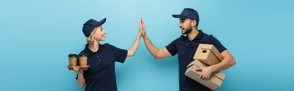 веселые межрасовые курьеры дают пять, держа кофе, чтобы пойти и коробки на синий, баннер