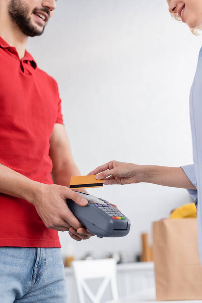 partial view of smiling delivery man holding payment terminal near woman with credit card