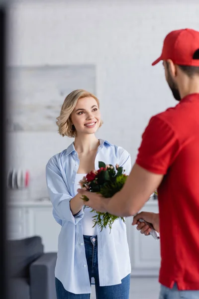 muslim delivery man giving bouquet to joyful woman, blurred foreground