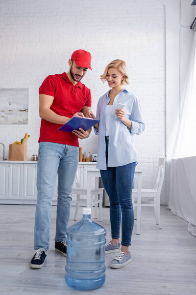 улыбающаяся женщина и арабский курьер стоят рядом с бутылкой питьевой воды