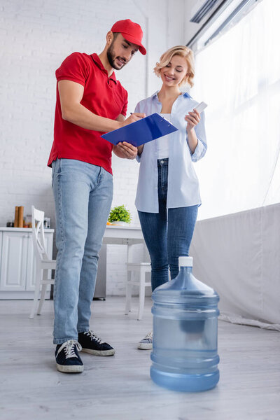 Мусульманский курьер пишет на планшете рядом с блондинкой и большой бутылкой воды