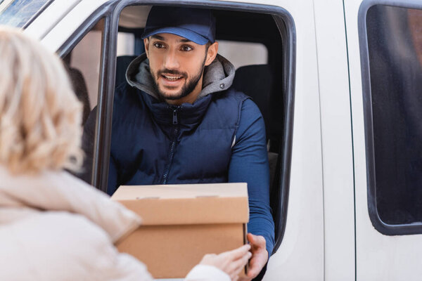 smiling muslim delivery man giving parcel to client on blurred foreground