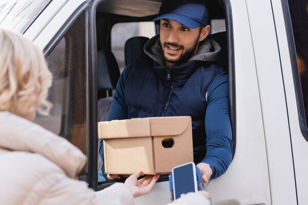 arabian postman holding box and payment terminal near woman with mobile phone on blurred foreground