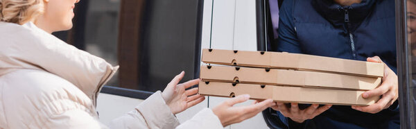 cropped view of woman taking pizza boxes from delivery man in car, banner