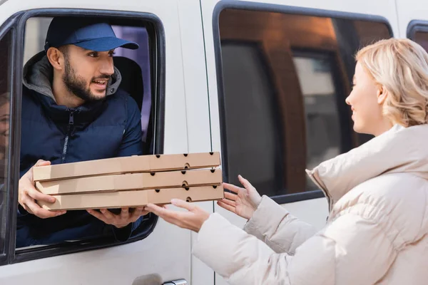 arabian delivery man in truck giving pizza boxes to blonde woman