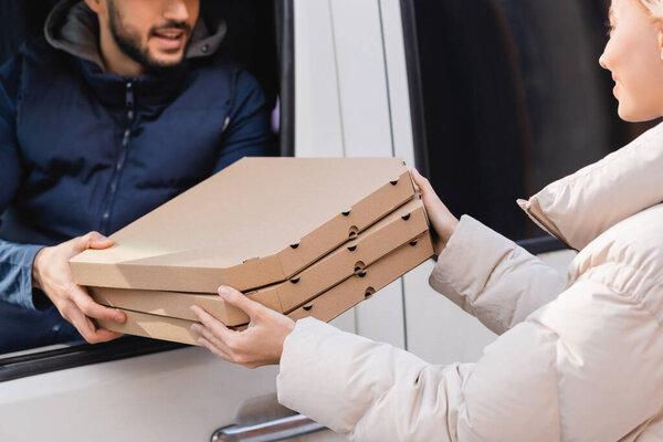 partial view of courier in car giving pizza boxes to woman on blurred background
