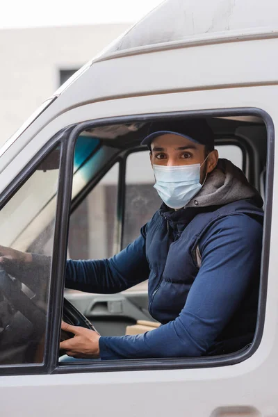 車に座っている間にカメラを見ている保護マスクのイスラム教徒の郵便配達人 — ストック写真