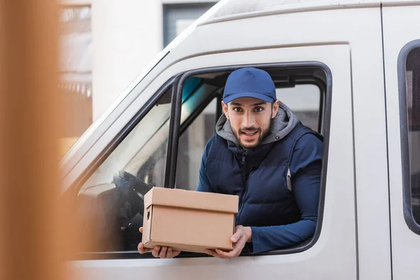 Positive Delivery Man Holding Parcel While Looking Out Car Window — Stock Photo, Image