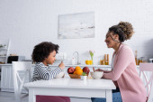 oldalnézetben afro-amerikai anya és lánya nézi egymást reggeli közben