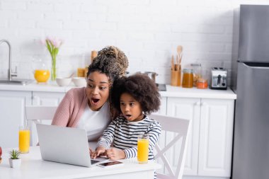 Şaşırtıcı bir şekilde Afrikalı Amerikalı anne ve kız laptop 'da portakal suyu bardaklarının yanında film izliyorlar.