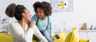 Mutlu bir Afro-Amerikan kadını ve kızı evde birbirlerine gülümsüyor.