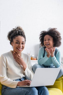 Afro-Amerikan kadın bilgisayarın yanında kameraya gülümsüyor ve gülüyor.