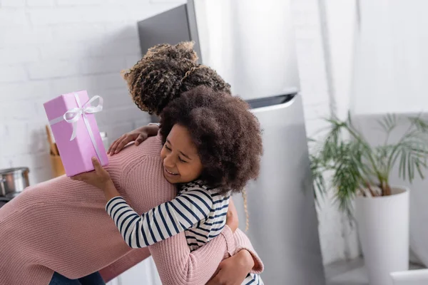 Afro Americana Mulher Abraçando Alegre Filha Segurando Mães Presente Dia — Fotografia de Stock