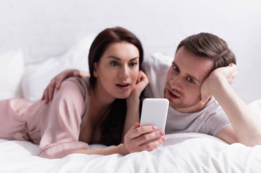 Cep telefonu, bulanık arka planda, kocasının yanında uzanan bir kadının cep telefonu. 