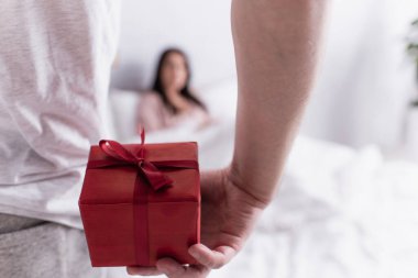 Kırmızı hediye kutusu elinde bulanık karısının yanında duran adamın elinde. 