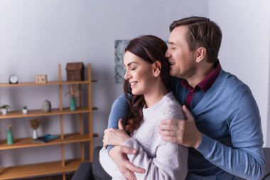 Gülümseyen adam evde eşine sarılıyor. 