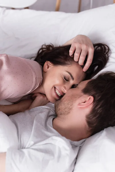 在睡衣中微笑的女人躺在丈夫身边的白色被褥上 — 图库照片